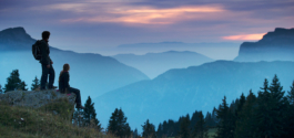 Male and female hikers looking out over the ridge towards the sunset and fading mountain lines in the background. Ross Woodhall - Action & Lifestyle Photography