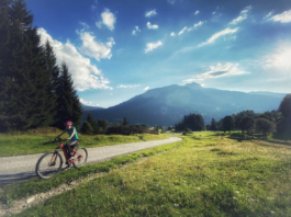young women on an electric ebike mountain bike, cycling along a dusty road with some pines and mountains in the background. Ross Woodhall - Action & Lifestyle Photography