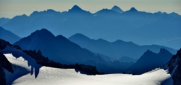 Outline of mountains in different shades of blue. With foreground crest of mountain covered in snow. Ross Woodhall - Action & Lifestyle Photography
