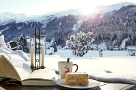 Outdoor sitting area with a book open by a slice of cake and a mug with a snowy backdrop. Ross Woodhall - Action & Lifestyle Photography