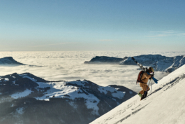 Lone skier, hiking up a snowy mountain with skis over his shoulders with clouds hugging the mountains, below him & in the background. Ross Woodhall - Action & Lifestyle Photography