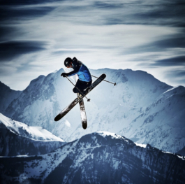 Skier in air crossing skis with mountains in background Ross Woodhall - Action & Lifestyle Photography